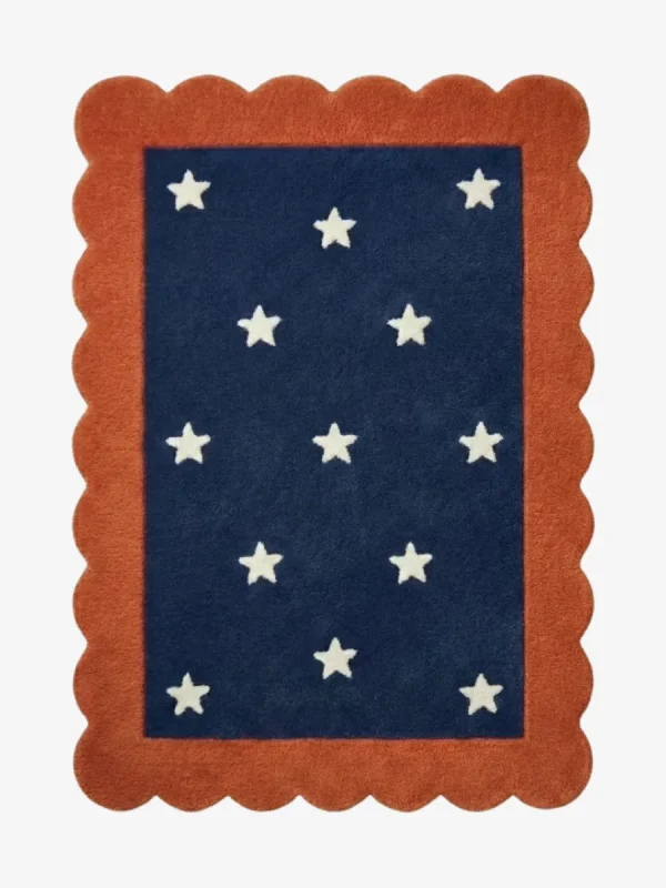 Top down view of the Cosmic Constellation rug featuring a deep navy blue rectangular center with a white star pattern, completely surrounded by a decorative rust orange scalloped border.