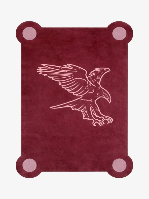 Top down view of the Ember Crest rug featuring a deep maroon wool background with a stylized light pink line art illustration of an eagle in flight, framed by decorative circular corner accents.