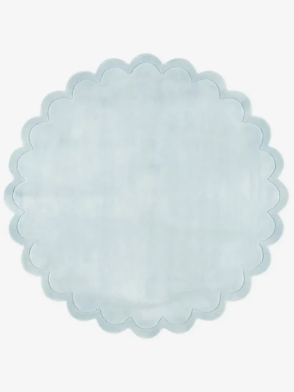Top down flat lay view of the Ice Whisper round rug showing the soft light blue wool color and scalloped border.