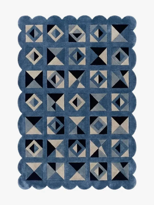 Top down view of the Indigo Tessellate rug against a white background, featuring a repeating patchwork pattern of geometric squares, triangles, and diamonds in solid shades of indigo blue, grey, and black, framed by a continuous blue scalloped border.