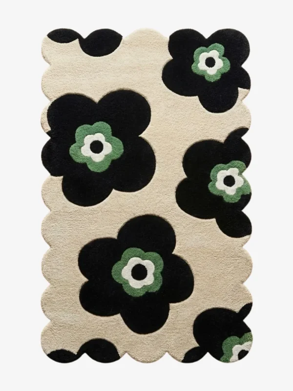 Top down flat lay of the Inked Botanica rug featuring bold black floral silhouettes with sage green centers on a beige wool background.
