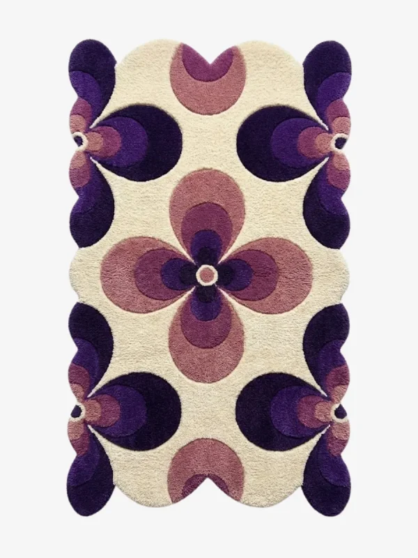 Top down flat lay of the Nocturne Bloom rug featuring a retro geometric floral pattern with dark purple and lilac petals on a cream wool background.