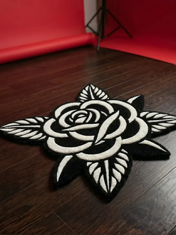 Angled view of the Noir Rose black and white flower rug placed on a dark wood floor in a photography studio setting, featuring a vibrant red seamless paper backdrop unrolled in the background.