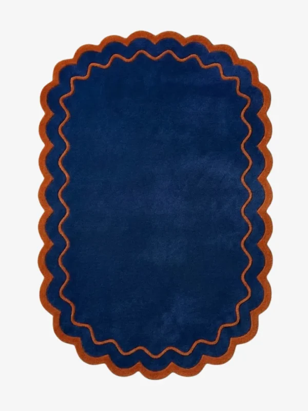 Top down view of the Ocean Garnet rug featuring a solid deep navy blue center framed by a rust orange wavy scalloped border.