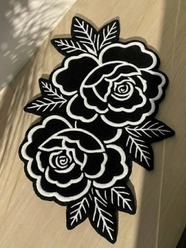 Top-down angled view of the Petal Duet black and white traditional tattoo rose rug bathed in striking natural sunlight and shadows on a light wooden floor.