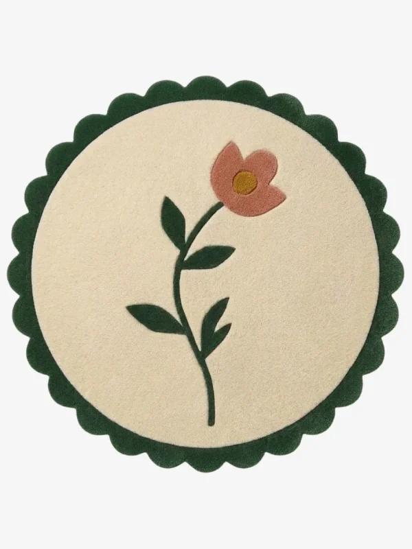 Top-down view of the circular Petal Poise rug, featuring a soft cream background adorned with a stylized pink flower and green stem, perfectly framed by a thick forest green scalloped border.