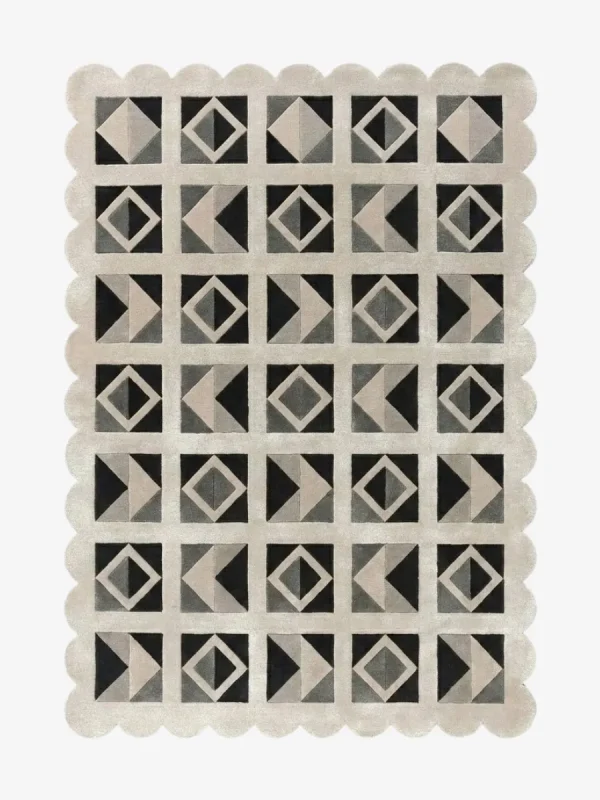 Top down view of the Shadow Grid rug against a white background, featuring a repeating patchwork pattern of geometric squares, triangles, and diamonds in shades of black, dark grey, light grey, and cream, framed by a continuous cream scalloped border.