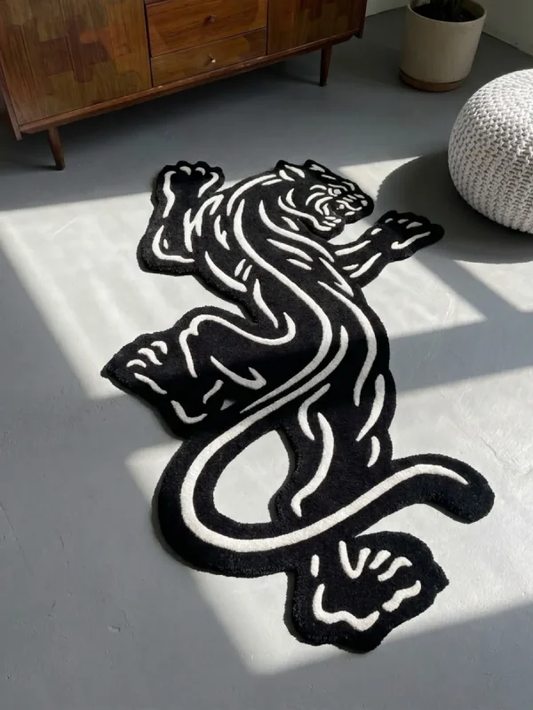 Perspective view of the Black Veil black and white traditional tattoo rose rug styled on a wooden floor in a living room next to a classic black fireplace, a potted plant, and a light grey leather sofa.