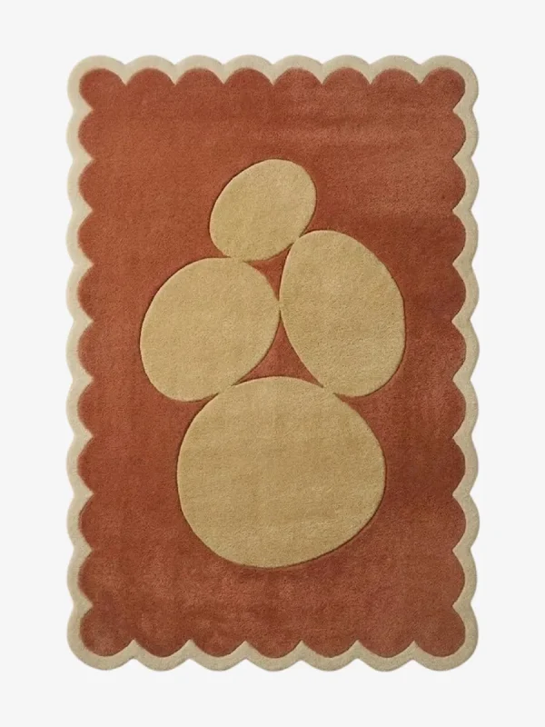 Top-down view of the rectangular Sienna Forms rug, featuring an abstract cluster of organic cream pebble shapes set against a warm rust orange field and framed by a matching cream scalloped border.