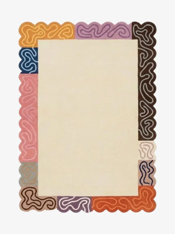 Top down view of the Soft Frame rug featuring a large neutral cream wool center framed by a playful multicolored border of striped blocks in pink, orange, brown, and purple, finished with custom scalloped edges.