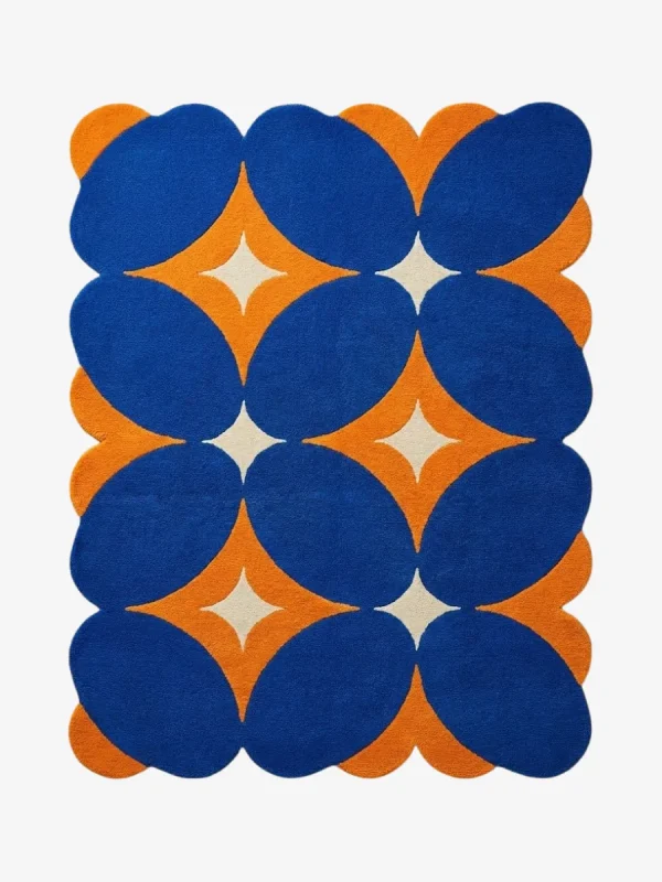 Top down flat lay of the Solar Indigo rug featuring a bold geometric pattern with deep blue ovals and vibrant orange diamond shapes on a cream background.