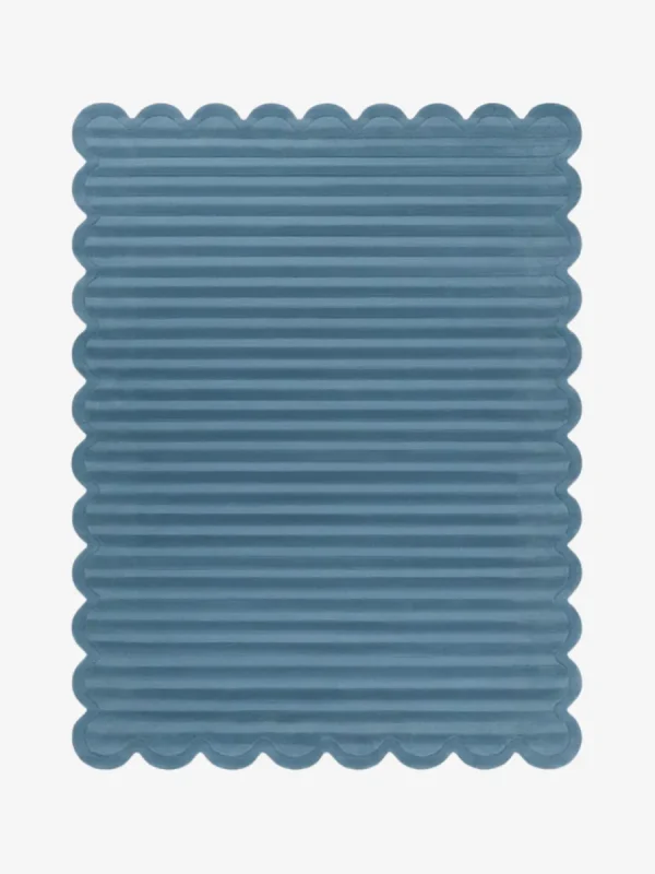 Top down view of the Still Tides rug featuring a solid dusty blue color with horizontal carved textures and decorative scalloped edges.