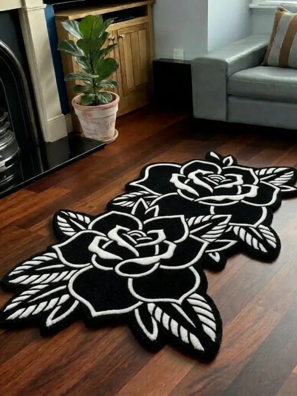 Perspective view of the Twin Ink Rose black and white double flower tattoo rug styled on a dark wood floor in a living room next to a potted plant, a black fireplace, and a light grey sofa.