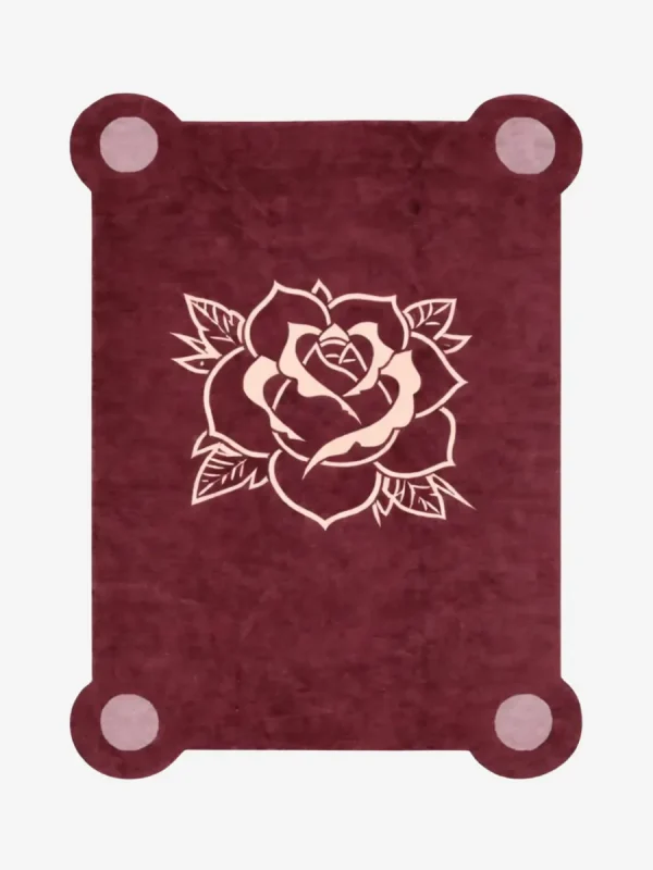 Top down view of the Velvet Bloom rug featuring a deep maroon wool background with a central traditional tattoo-style rose illustration in light pink and cream, framed by decorative pink corner accents.