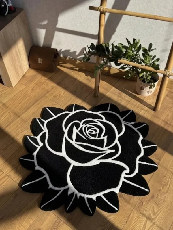 Perspective view of the Void Blossom black and white rose-shaped rug styled on a light hardwood floor in a sunlit room, next to a potted plant and a wooden ladder shelf.